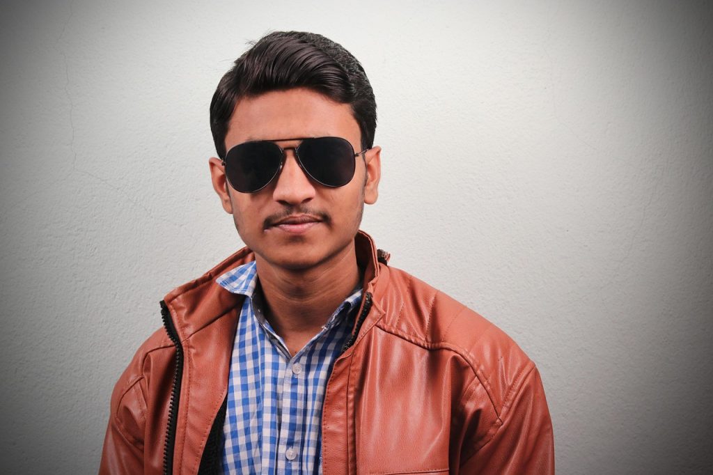 CA student standing outdoors wearing a brown jacket and sunglasses